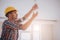 Handsome young builder in a yellow construction helmet is twisting the light bulb in. The man is looking up .