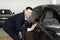 Handsome young businessman in classic blue suit is smiling while examining car in a motor show.