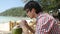 Handsome young businessman in sunglasses drink fresh coconut juice in a beach cafe with sea view on palm trees on