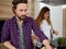 Handsome young Caucasian man preparing meal with her pregnant woman out of focus on the background at home kitchen