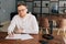 Handsome young composer wearing stylish eyeglasses is sitting at the desk with paper sheet music