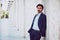 Handsome young elegant man posing outdoors along a corridor of white columns. Fashionable hair wearing jacket, pants and shirt