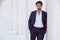 Handsome young elegant man posing outdoors leaning on a column along a corridor. Fashionable hair.