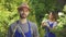 Handsome young farmer in blue robe standing in the foreground while his wife watering trees in the background. Male and