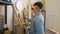 Handsome young hispanic man, a dedicated carpenter, standing in his bustling workshop, gripping a timber plank for furniture