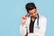 Handsome young Indian / Asian doctor with a stethoscope, in a white coat, is poking about a problem on a blue background