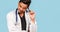 Handsome young Indian / Asian doctor with a stethoscope, in a white coat, is poking about a problem on a blue background