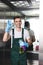 handsome young janitor holding spray bottle with detergent and rag smiling at camera and showing ok sign