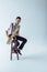 handsome young jazzman sitting on stool and playing saxophone