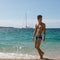 Handsome young man in a bathing suit comes out of the sea on the