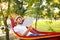 Handsome young man with book resting in hammock outdoors