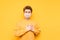Handsome young man in bright clothes and a medical mask on his face stands on a yellow background and shows a gesture of love,