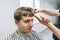 Handsome young man clipping in barber shop, closeup portrait. Hairdresser trims the hair with scissors on the head of a positive