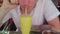 A handsome young man drinks a healthy orange smoothie in a tropical cafe. The guy drinks a fresh juice or cocktail.