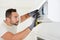 Handsome young man electrician cleaning air filter on an indoor unit of an air conditioning in a client house