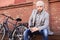 Handsome young man in grey coat and hat sitting on a bench relaxed drinking coffee and thinking near his bicycle