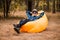 Handsome young man in hat and sunglasses lying on inflatable sofa with hands up and enjoy free time on open air