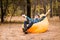 Handsome young man in hat and sunglasses lying on inflatable sofa with hands up and enjoy free time on open air while resting on