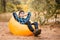 Handsome young man in hat and sunglasses lying on inflatable sofa with hands up and enjoy free time on open air, while resting on