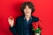 Handsome young man holding bouquet of flowers and engagement ring smiling and laughing hard out loud because funny crazy joke
