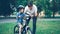 Handsome young man loving father is teaching his small son to ride bicycle in park on summer day, boy is riding bike