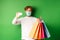 Handsome young man in medical mask, showing plastic credit card and shopping bags with items purchased with discount