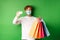 Handsome young man in medical mask, showing plastic credit card and shopping bags with items purchased with discount