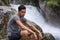 Handsome young man near mountain waterfall on rock