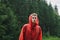 Handsome young man in a red raincoat in the mountains in the rain, looks into the camera with a serious face. Mountain downpour in