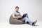 Handsome young man sitting on a bean bag putting his laptop on his legs and working isolated on white background