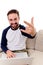 Handsome young man sitting on couch showing gestures with palm.