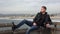 Handsome young man sitting on the edge of a pier over the ocean