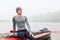 Handsome young man sitting on his canoe after rowing on kayak, happy sportsman having rest after long hours padding, wearing