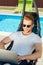 handsome young man sitting in sun lounger in front of swimming pool and working