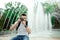 Handsome young man taking photo in park. Stylish boy in a white t-shirt, with bagpack taking photos in front of amazing fountain