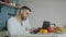 Handsome young man talking phone and using laptop computer sitting in the kitchen after breakfast in the morning