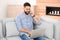 Handsome young man talking on phone while working with laptop on sofa