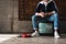 handsome young man in vintage clothes sitting on retro tv set near red wired telephone in front of rug hanging