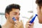 Handsome young man wearing black singlet top looking in mirror, using shaving device during morning routine concept