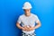 Handsome young man wearing builder uniform and hardhat with hand on stomach because indigestion, painful illness feeling unwell