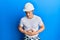 Handsome young man wearing builder uniform and hardhat with hand on stomach because nausea, painful disease feeling unwell