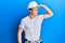 Handsome young man wearing builder uniform and hardhat very happy and smiling looking far away with hand over head