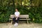 Handsome young man in white T-shirt and black trousers sitting on the wooden bench in the park waiting impatiently for someone to