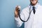 Handsome young medic holding a stethoscope, isolated over light blue.