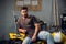 A handsome young motorcyclist in jeans and a t-shirt poses for a photo sitting on a bike in his garage