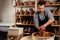 Handsome young potter man in a gray sweater and a black apron sculpts clay pot on a potter`s wheel in a cozy craft