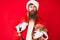 Handsome young red head man with long beard wearing santa claus costume holding teddy bear relaxed with serious expression on face