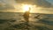 A handsome young surfer is sitting on a board in the ocean and waiting for a wave while enjoying the sunset. The