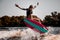 Handsome young woman skillfully jumping over splashing river wave on surf style wakeboard.