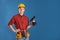 Handsome young working man with electric drill against color background